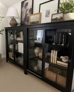 a black bookcase with glass doors and pictures on the wall behind it in a living room