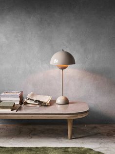 a table with books and a lamp on it in front of a gray wall,