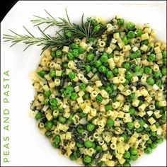 a white plate topped with pasta and peas next to a sprig of rosemary