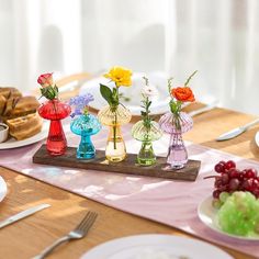 small vases filled with colorful flowers sit on a table next to plates and silverware