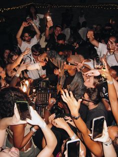 a group of people holding up cell phones in front of a dj's booth