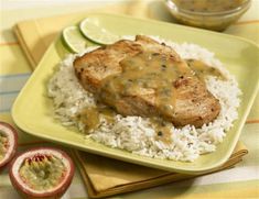 a green plate topped with rice and meat covered in gravy next to sliced kiwi