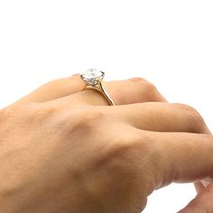 a person's hand holding an engagement ring with a diamond in the middle, against a white background