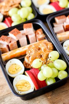 two black trays filled with different types of food on top of a wooden table