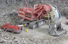 there is a large red machine in the middle of some rocks and gravel with other vehicles around it