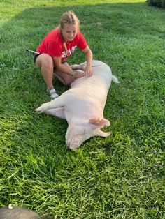 a woman kneeling down next to a pig on top of a lush green grass covered field