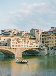 a small boat floating on top of a river under a bridge with buildings in the background