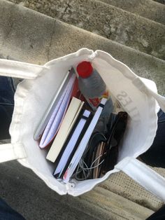 a white bag filled with books and other items sitting on top of cement steps next to a person's legs