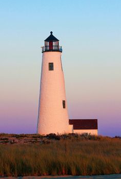 a white lighthouse sitting on top of a grass covered hill next to a body of water