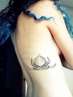 the back of a woman's body with a tattoo on her left shoulder and seashell