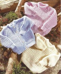 three knitted sweaters sitting next to each other on top of a pile of logs