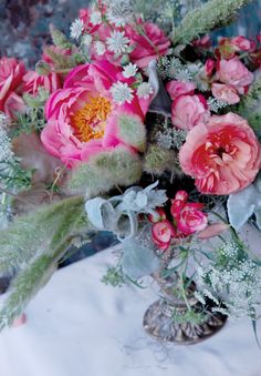 a vase filled with lots of pink flowers on top of a white cloth covered table