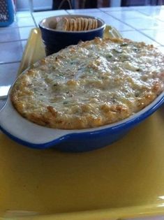 a casserole dish on a yellow table with a bowl of crackers next to it