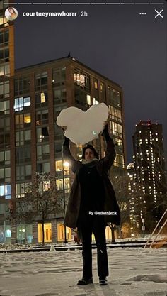 a woman holding up a heart shaped object in front of a large building at night