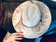 🌙✨ Embrace celestial elegance with our handcrafted light beige wide brim hat, intricately adorned with a mystical moon and sun design and embellished with healing crystals. Each hat is carefully hand burned to create a unique and enchanting piece that exudes mystic energy. 🔮 Our wide brim hat is the perfect accessory to elevate your style while embracing the healing powers of crystals. The combination of the moon and sun motifs symbolizes balance, harmony, and spiritual alignment, making this hat not only a fashion statement but a powerful talisman for your everyday wear. 🌟 Made with high-quality materials and attention to detail, this wide brim hat is a one-of-a-kind piece that will surely turn heads and spark conversations wherever you go. Whether you're a bohemian soul, a lover of as Artisan White Hat Bands For Summer, Unique Summer Fedora With Curved Brim, Artisan White Fedora For Festivals, Handmade Unique Hat Bands For Summer, Handmade White Bohemian Fedora, Custom White Festival Hat, White Artisan Sun Hat With Flat Brim, Artisan White Sun Hat With Flat Brim, Summer Festival High Crown Hats