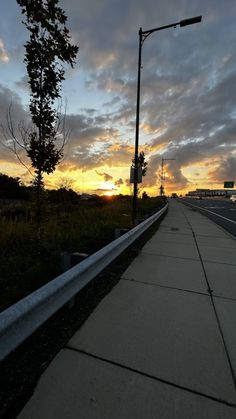 an empty sidewalk next to a street with the sun setting in the sky behind it