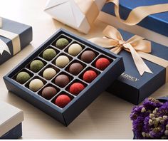 an assortment of chocolates in a gift box on a table with purple flowers and blue boxes