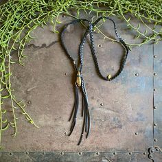 "-This showstopper necklace is made from braided black deerskin leather and a gold-painted quartz crystal. -An original blend of boho, hippie, rocker, and pagan aesthetics with a nod to Jack Sparrow, this necklace is sure to be a conversation piece. -The gold stone is a painted quartz, and each is unique. -The tassel is accented with a couple African brass beads. -Necklace length to the pendant is about 30.\" Stone and tassel are about 7\" combined. -Designed and handmade in South Pasadena, CA. Bohemian Gold Necklaces For Everyday Use, Black Jewelry With Adjustable Length For Everyday, Black Waxed Cord Jewelry For Everyday Use, Black Adjustable Necklace For Everyday Use, Adjustable Black Necklace For Everyday Use, Handmade Black Leather Necklace, Bohemian Braided Leather Jewelry, Black Bohemian Lariat Necklace, Black Brass Necklace For Festival