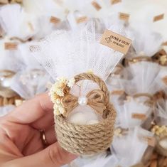 a hand holding a rope wrapped candle holder with flowers and pearls on it's side