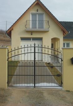 a yellow house with a black gate and fenced in area next to the driveway