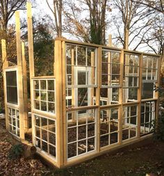 a wooden structure with glass windows in the middle of some grass and leaves on the ground