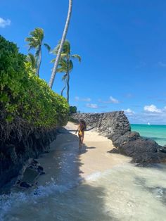 a woman walking on the beach with palm trees in the background