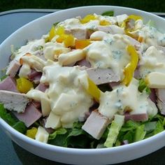 a salad with chicken, cheese and peppers in a white bowl on a blue table