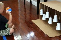 a little boy sitting on the floor playing with a ball in front of some cups