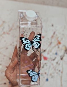 a hand holding a plastic bottle with two butterflies on it