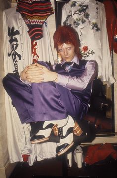 a man with red hair sitting on top of a chair in front of some clothes