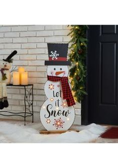 a snowman with a hat and scarf standing in front of a christmas tree, next to a door