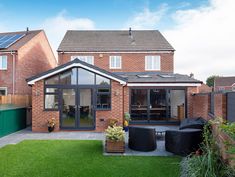 a brick house with an enclosed back yard and patio area in the foreground, surrounded by green grass