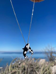 a black and white orca whale necklace hanging from a silver chain with ocean in the background