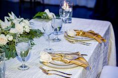 the table is set with white flowers and gold place settings for two people to sit at