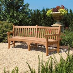 a wooden bench sitting on top of a gravel field next to trees and flowers in a potted planter