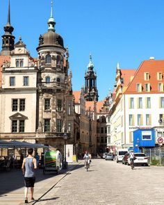 people are walking down the street in an old european city with tall buildings on either side