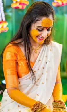 a woman with yellow paint on her face and hands, sitting in front of flowers