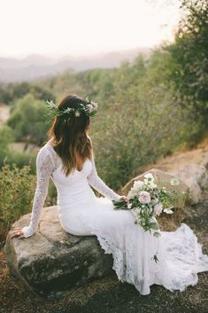 a woman sitting on top of a rock wearing a white dress and holding a bouquet