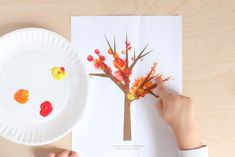 a child's hand is holding a paper plate with an autumn tree on it