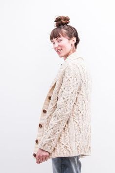 a woman standing in front of a white wall wearing jeans and a cardigan sweater