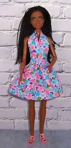 a barbie doll wearing a dress with flowers on it and pink shoes, standing in front of a white brick wall