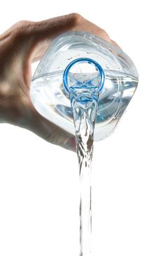 a hand is pouring water from a pitcher into a glass cup with a blue handle