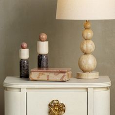 a white dresser topped with lots of different types of items next to a lamp on top of it