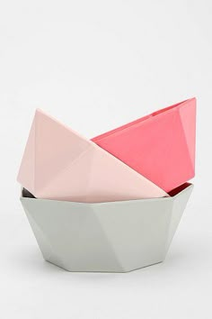 three different colored paper boats sitting in a bowl on a white surface with one red and one pink