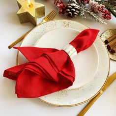 a red napkin sits on top of a white plate next to gold forks and silverware