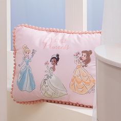 a pillow with princesses on it sitting next to a window sill in a room