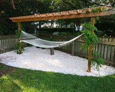 a hammock is in the middle of a yard with gravel and plants around it