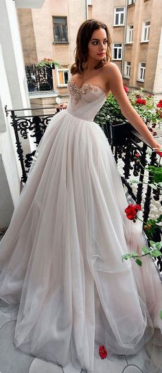 a woman in a white wedding dress standing on a balcony with red flowers and greenery