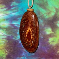 a wooden pendant is hanging from a chain on a colorful tie - dyed background,