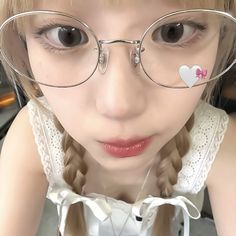 a girl wearing glasses with heart stickers on the side of her eye and looking at the camera